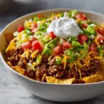 A close-up view of a hearty taco salad layered with seasoned ground beef, shredded cheese, lettuce, tomatoes, and sour cream.