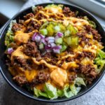 A close-up of a delicious cheeseburger bowl featuring seasoned ground beef, melted cheese, special sauce, pickles, and red onion over lettuce.