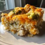 A close-up serving of creamy chicken broccoli rice casserole topped with melted cheddar cheese.