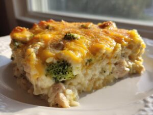 A close-up slice of creamy chicken broccoli rice casserole topped with melted cheddar cheese.