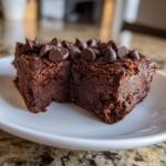 A close-up of a fudgy Cottage Cheese Microwave Brownie topped generously with chocolate chips, sitting on a white plate.