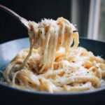 Close-up of fettuccine pasta coated in rich homemade alfredo sauce being lifted by a fork.