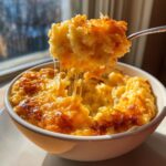 A spoonful of creamy Southern cheese grits showing a dramatic cheese pull, served in a white bowl.
