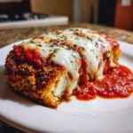 Close-up of a piece of Easy Chicken Parmesan, breaded, topped with melted mozzarella, marinara sauce, and herbs.