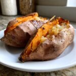 Two perfectly cooked baked sweet potatoes, split open to show the fluffy orange interior.