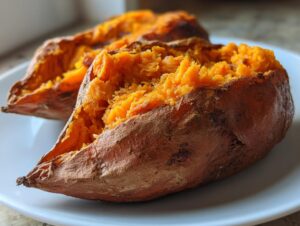 Two perfectly baked sweet potatoes, split open to reveal fluffy, bright orange flesh.
