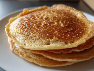 A close-up stack of three golden-brown sourdough pancakes showing many small bubbles on the top surface.