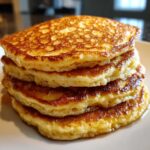 Close-up of a tall stack of four fluffy sourdough pancakes, golden brown and glistening with syrup.