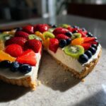 A slice removed from a vibrant fruit pizza sugar cookie topped with strawberries, kiwi, blueberries, and oranges.