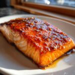 Close-up of a perfectly cooked salmon fillet topped with a thick, shiny, orange-brown glaze.