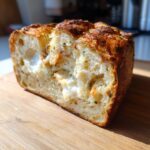 Close-up of a freshly baked Italian herb and cheese bread loaf, showing a soft, cheesy interior and golden crust.