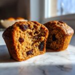 Close-up of moist bran muffins, one cut in half revealing a tender crumb dotted with raisins.