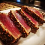 Four thick slices of perfectly seared ahi tuna, crusted with sesame seeds, showing a bright pink raw center.