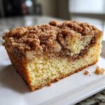 Close-up of a moist slice of coffee cake showing the yellow cake base, cinnamon swirl, and thick brown sugar crumb topping.