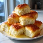 A tempting stack of soft, freshly baked dinner rolls piled high on a white plate, glistening with melted butter.