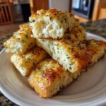 A pile of soft, fluffy breadsticks topped with melted cheese and green herbs, showing the airy interior.
