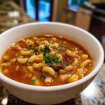 Close-up of a white bowl filled with rich, tomato-based pasta fagioli soup, topped with fresh parsley.