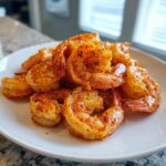 A close-up of perfectly cooked, seasoned air fryer frozen shrimp piled high on a white plate.