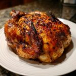 A whole roasted chicken with deeply browned, crispy skin, seasoned with pepper, ready to serve after being cooked as an air fryer whole chicken.