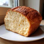 A close-up of a loaf of golden-brown beer bread, sliced to show its fluffy, airy interior texture.