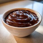 A close-up of thick, glossy, dark brown chocolate dip swirled in a small white bowl.