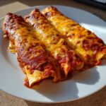 Three freshly baked cheese enchiladas covered in rich red sauce and melted golden cheese.