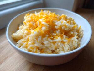 A close-up of creamy, white rice topped generously with shredded cheddar cheese, showcasing the amazing cheesy rice.