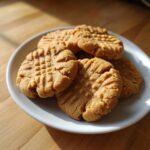 A small stack of golden brown peanut butter cookies with classic crosshatch fork marks on a white plate.