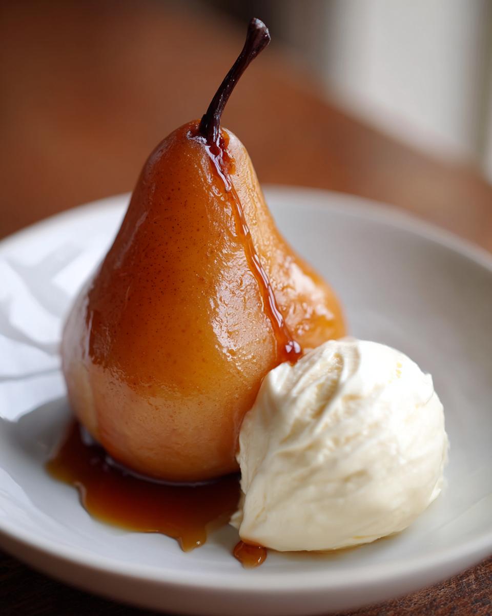 A close-up of a perfectly caramelized poached pears dessert served with a scoop of vanilla ice cream on a white plate.