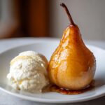A perfectly glazed poached pear served next to a scoop of vanilla ice cream on a white plate.