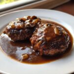 Two perfectly cooked salisbury steak patties smothered in rich brown mushroom gravy on a white plate.
