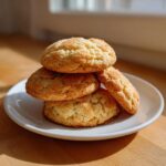 A stack of four golden brown, crinkly sugar cookie treats coated in sparkling sugar, resting on a white plate.