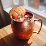 A frosty copper mug filled with an apple cider Moscow mule, garnished with thin apple slices.