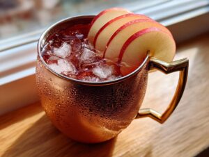 Close-up of a frosty copper mug filled with an apple cider Moscow mule cocktail, garnished with thin apple slices.