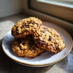 Three freshly baked banana oatmeal cookies with visible chocolate chips stacked on a small white plate.