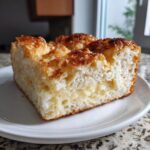 A thick slice of bee sting cake showing the fluffy white cake, creamy vanilla filling, and caramelized topping.