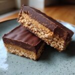 Close-up of two layered buckeye graham crackers bars featuring a crunchy base, peanut butter filling, and chocolate ganache topping.