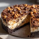 Close-up of a rich butterfinger pie with a dark crust, creamy filling, and generous topping of chocolate chunks and crushed candy.
