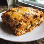 A square slice of cheesy chicken burrito bake with rice and beans on a white plate.