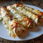 Three baked green chile chicken enchiladas covered in melted, browned cheese and herbs on a white plate.