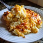 A fork lifts a portion of cheesy potato bake, showing melted cheese stretching between the fork and the casserole.