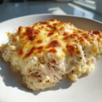A close-up serving of creamy chicken cauliflower rice casserole topped with bubbly, browned cheese.