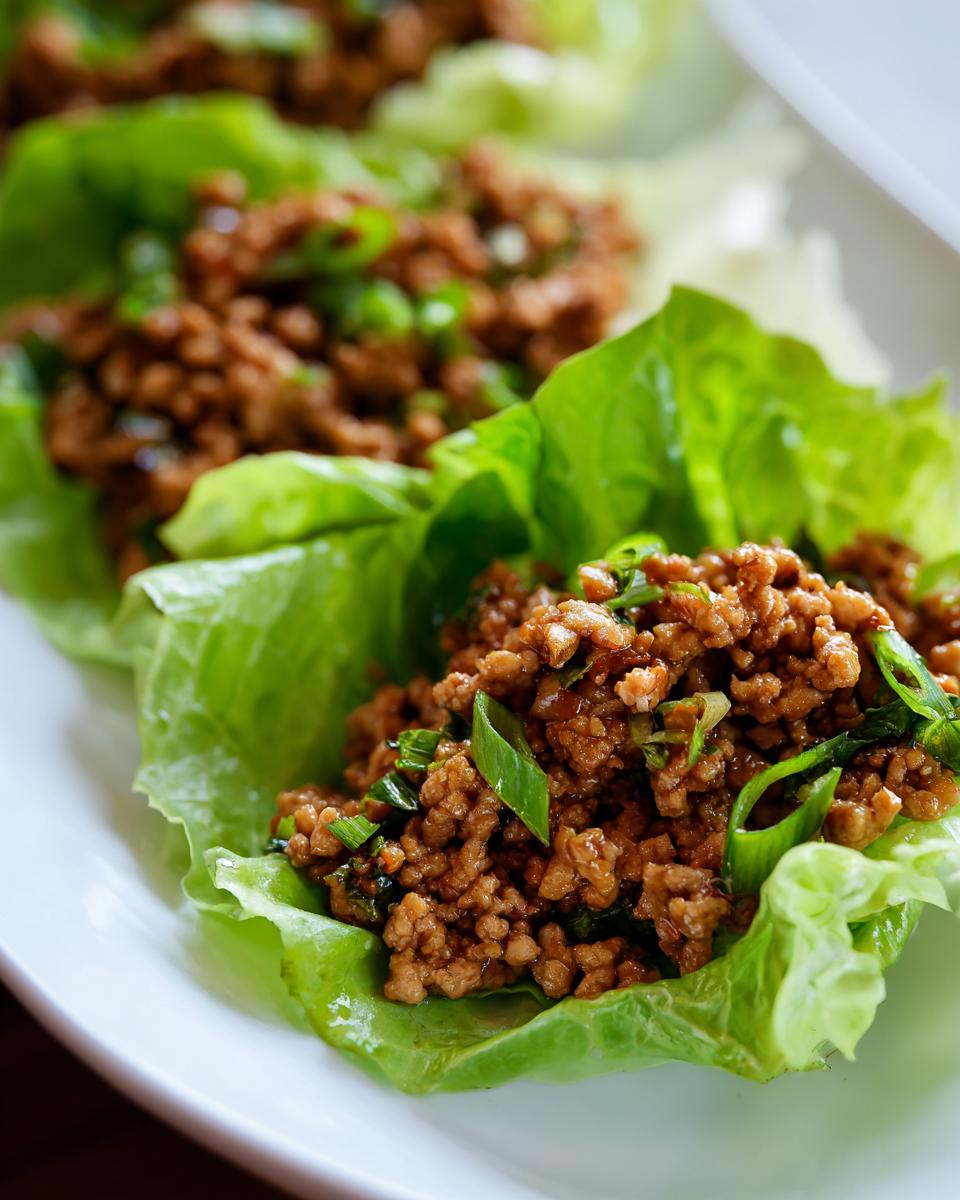 Close-up of savory ground chicken filling topped with green onions served in crisp lettuce cups for chicken lettuce wraps.