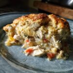 A close-up of a hearty serving of chicken pot pie casserole with creamy filling and a golden biscuit topping.