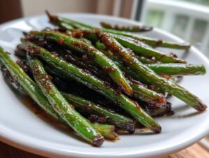 A close-up of vibrant, glossy chinese green beans with garlic sauce piled on a white plate.