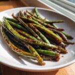A close-up of perfectly cooked chinese green beans with garlic sauce piled on a light-colored plate.