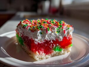 A festive slice of christmas poke cake featuring layers of white cake, red and green jello, whipped topping, and colorful sprinkles.