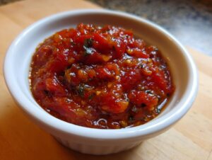 Close-up of chunky, vibrant red homemade pizza sauce seasoned with herbs, served in a small white ramekin.