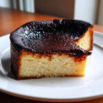A thick slice of creamy basque burnt cheesecake with a deeply caramelized, dark top, served on a white plate.
