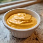 Close-up of a small white bowl filled with thick, creamy, orange-yellow beer cheese dip.
